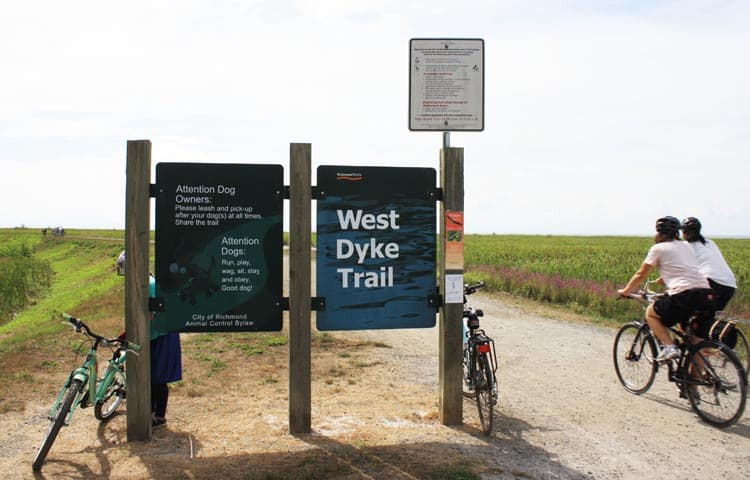 West Dyke Trail sign in Richmond with parked rental bikes and riders on the path